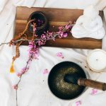 Meditation setup with a singing bowl, buda candle, beaded mala, and flower branch.