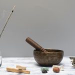 Arrangement of spiritual healing items including incense, bowl, sage, and gemstones on a marble surface.